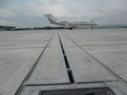 Caniveau a fente cf forte stradal integre dans piste aeroportuaire pour drainage des eaux pluviales avec avion en arriere plan